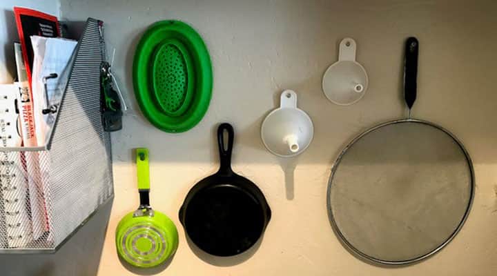 pots and pans and colander hanging on vertical space in kitchen wall